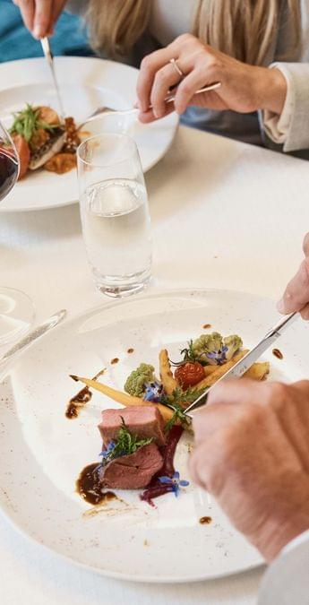 Elegant couple dining with gourmet meat dish, red wine, and refined table setting