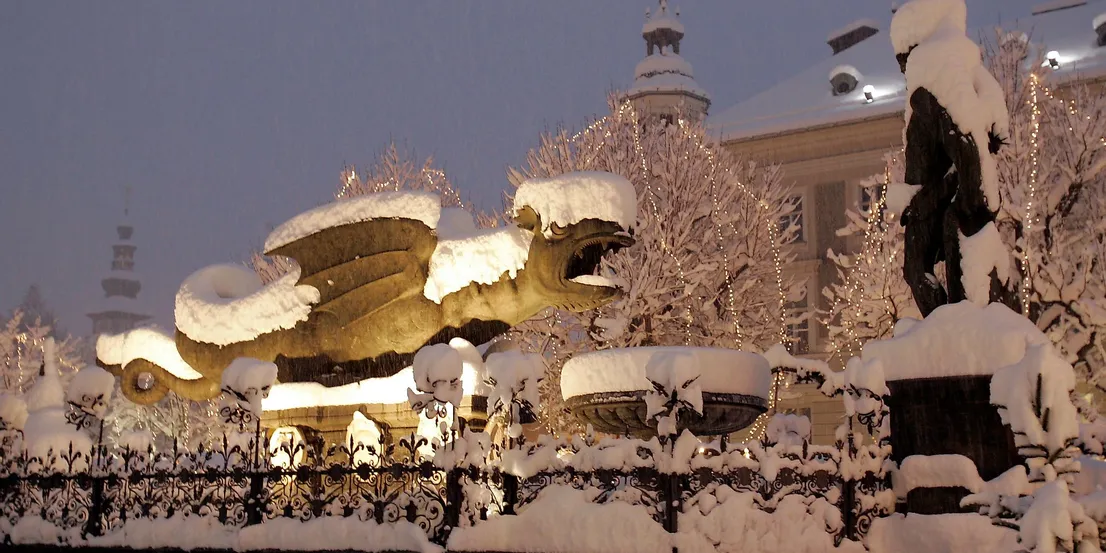 Schneebedeckter Drachenbrunnen in Klagenfurt an einem Winterabend