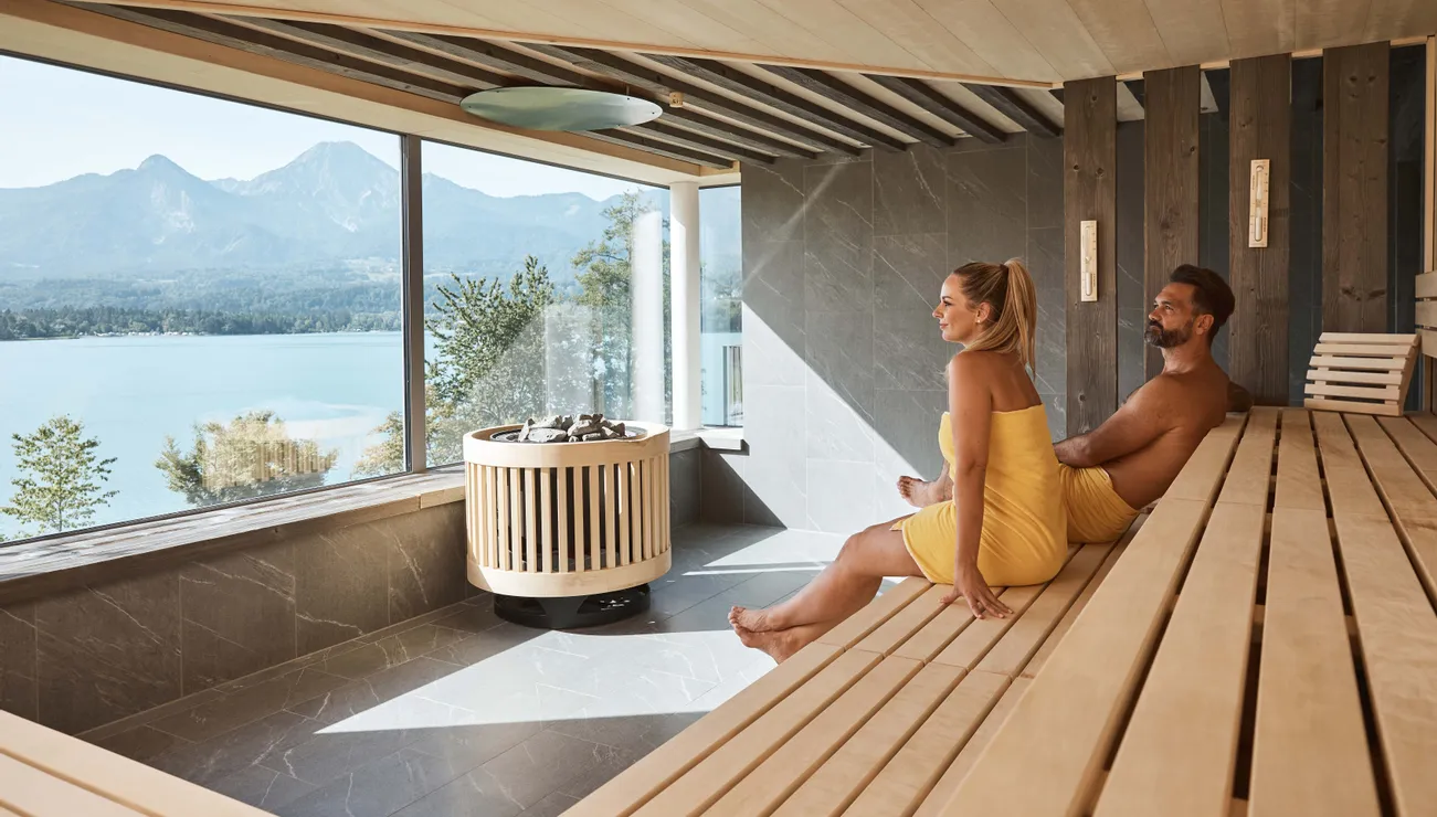 Paar entspannt in moderner Sauna mit Panoramablick auf See und Berge