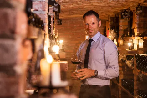 Man holding a glass of red wine in a warmly lit wine cellar