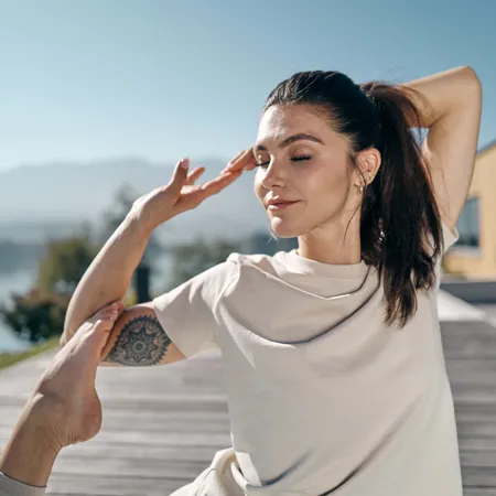 Donna che pratica yoga all'aperto in posizione seduta con lago e montagne sullo sfondo