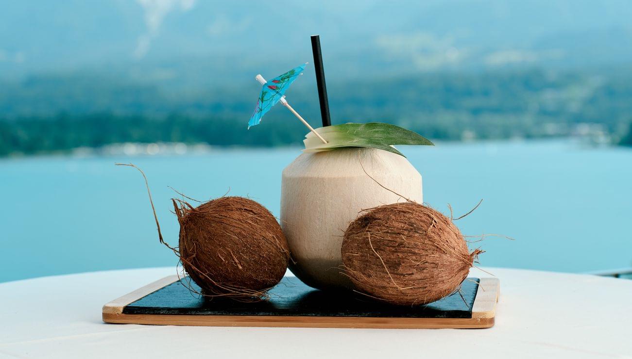 Frisches Kokosgetränk mit Schirmchen und zwei Kokosnüssen vor See- und Bergkulisse