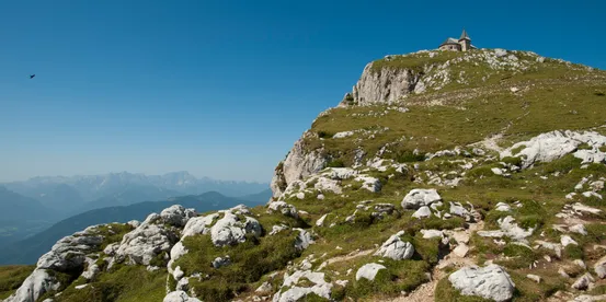 Cappella di montagna su pendio roccioso sotto cielo blu limpido in paesaggio alpino