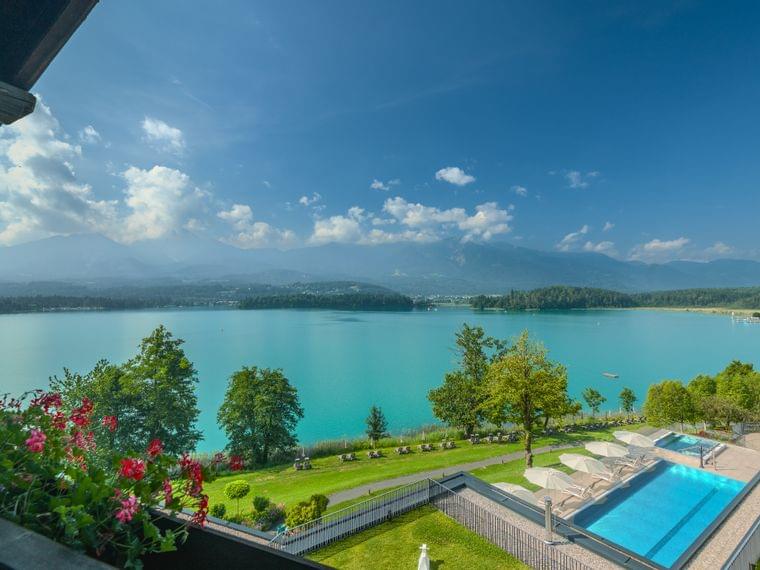 Panoramablick auf türkisfarbenen See, Berge, Pool und Garten vom Hotelbalkon
