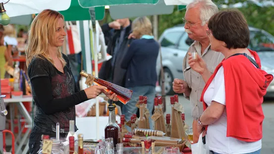 Frau verkauft Fruchtlikör an ein älteres Paar an einem Marktstand im Freien