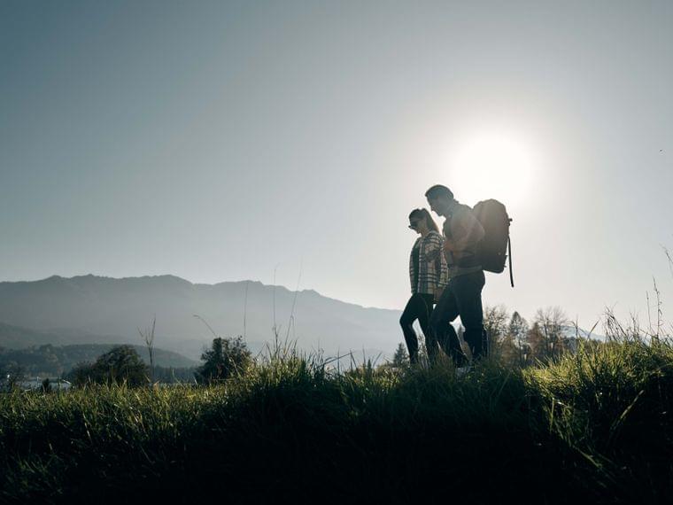 Couple hiking through grassy landscape with mountains in the background at sunset