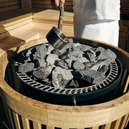 Wasser wird über heiße Saunasteine in einem hölzernen Saunaofen gegossen