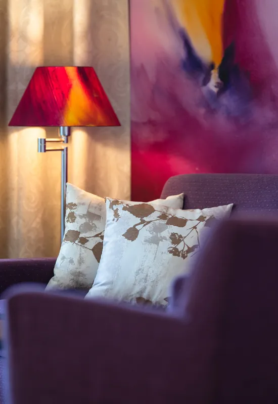 Moderne Hotellounge mit lila Sofa, abstrakter Wandkunst und roter Lampe