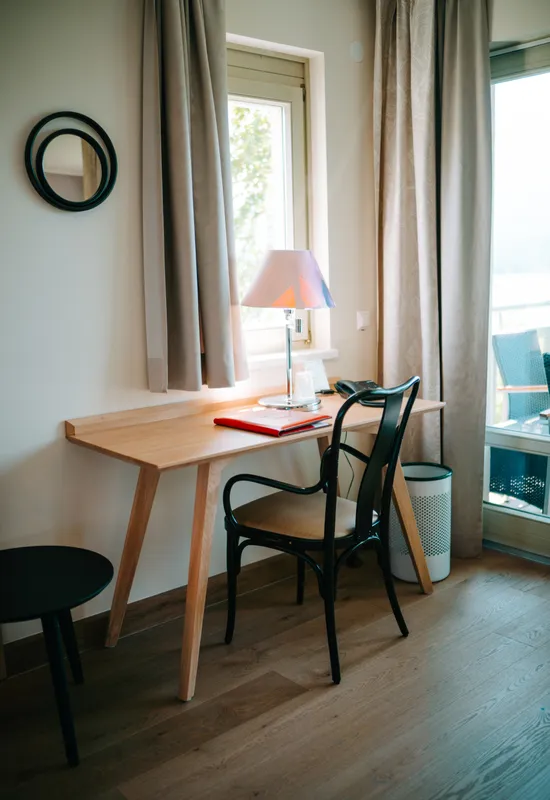 Gemütliche Homeoffice-Ecke mit Holztisch, schwarzem Stuhl, Lampe und Tageslicht vom Fenster