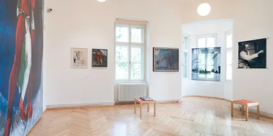 Bright art gallery room with wood floors displaying modern paintings and photographs on white walls