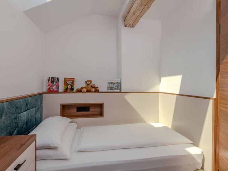 Minimalistisches Kinderzimmer mit Einzelbett, Teddybären und Büchern auf Holzregal