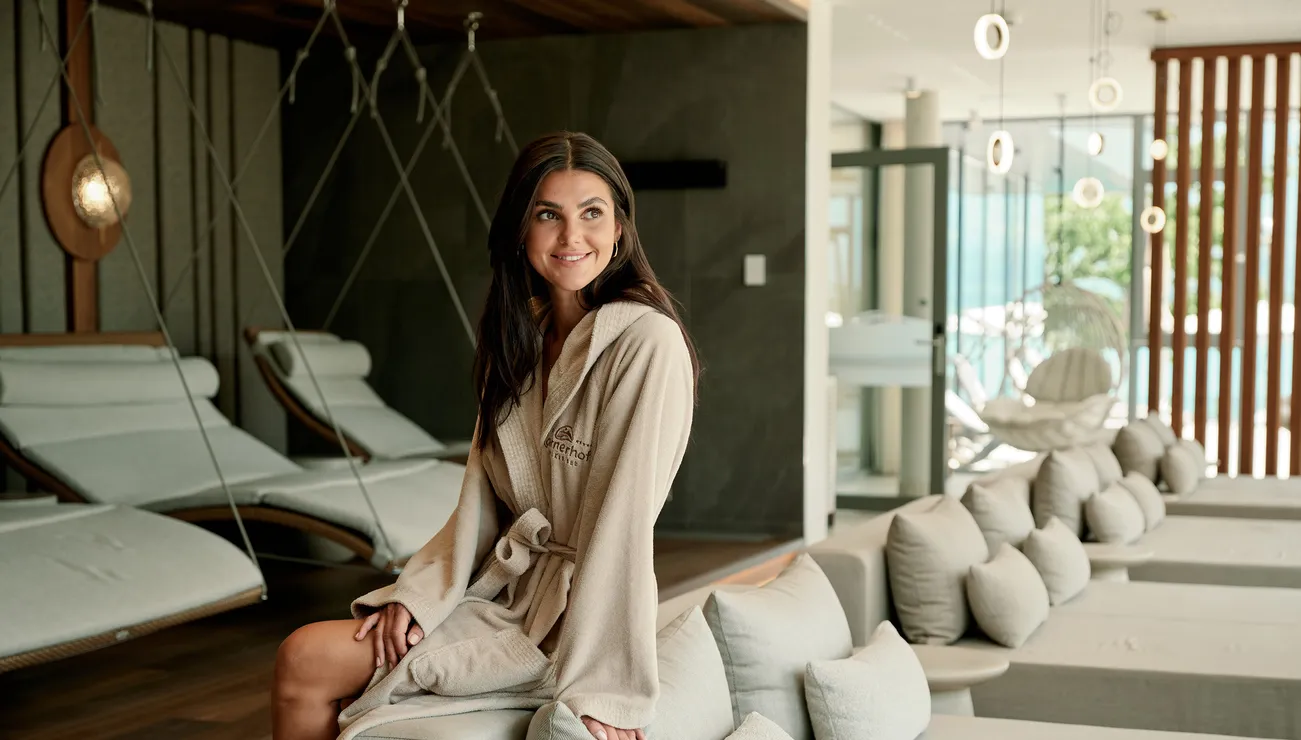 Donna in accappatoio beige rilassata nella lounge spa moderna con lettini imbottiti