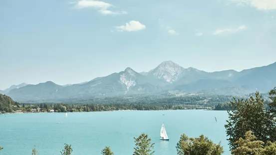 Segelboot auf türkisfarbenem Alpensee vor bewaldeten Bergen