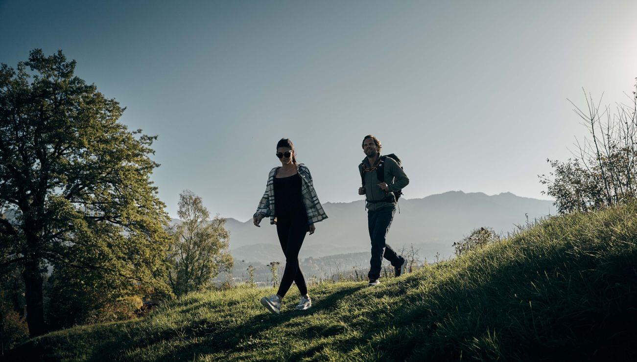 Paar wandert auf einem grasbewachsenen Hügel mit Bergen im Hintergrund