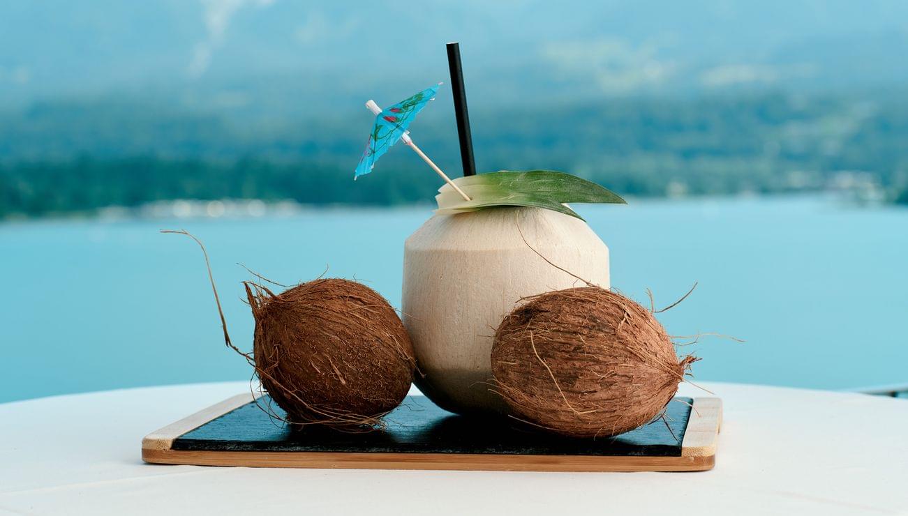 Fresh coconut drink with umbrella and two coconuts on table overlooking lake and mountains