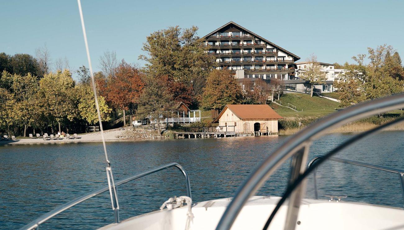 Blick vom Boot auf ein Seehotel mit Herbstbäumen und klarem Himmel