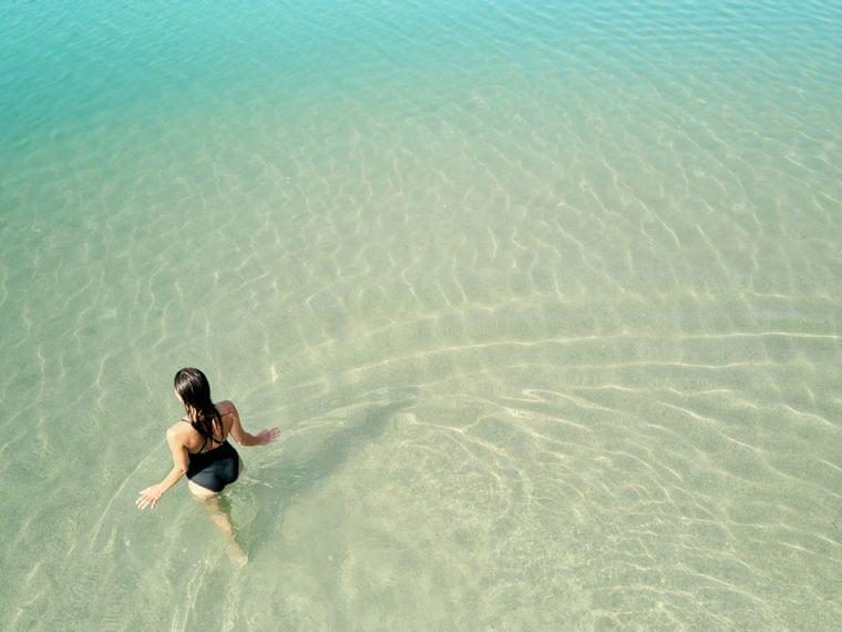 Donna in costume nero entra nel mare turchese trasparente su una spiaggia tropicale