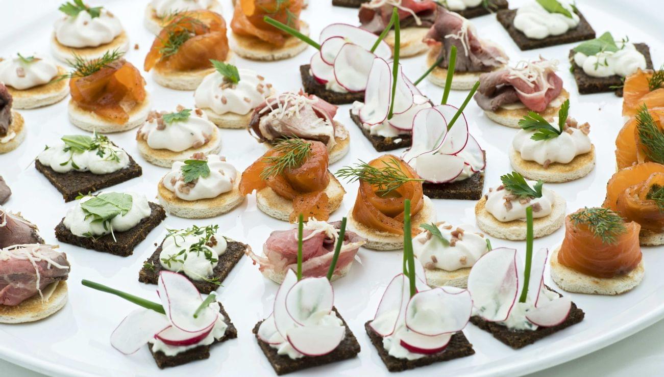 Assortimento di canapé gourmet con salmone affumicato, ravanelli, roast beef e crema su pane nero e bianco