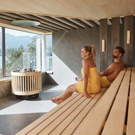 Paar entspannt in moderner Sauna mit Panoramablick auf See und Berge