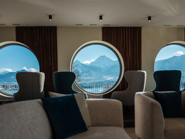 Lounge moderna con finestre circolari e vista panoramica sulle montagne alpine innevate