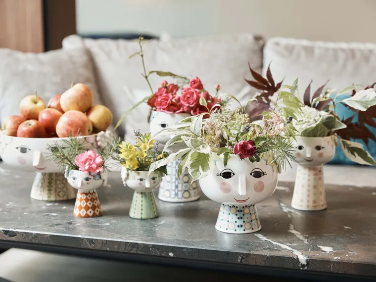 Decorative face-shaped ceramic vases with flowers and apples on a modern coffee table