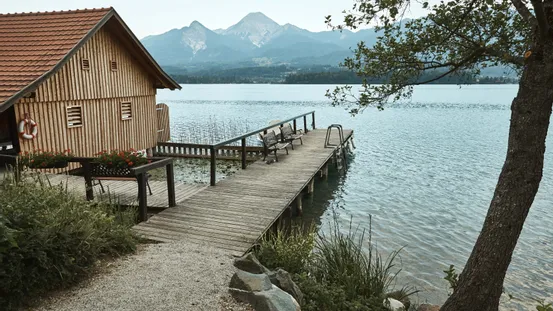 Holzbootshaus und Steg an ruhigem See mit Bergblick im Hintergrund