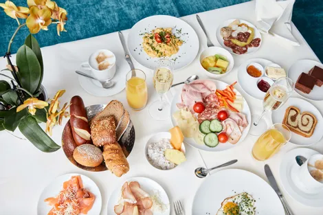 Kontinentales Frühstück mit Aufschnitt, Brot, Gebäck, Obst, Eiern und Getränken auf weißem Tisch