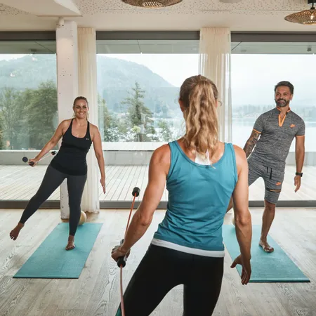 Lezione di fitness di gruppo con barre di resistenza in studio luminoso con vista lago