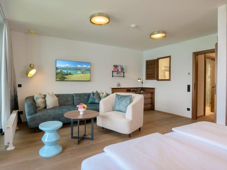 Modernes Hotelzimmer mit Sofa, Sessel, Schreibtisch, Fernseher und Holzfußboden