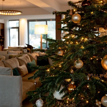Eleganter Weihnachtsbaum mit goldenen Kugeln und Lichtern in einer gemütlichen Hotellounge