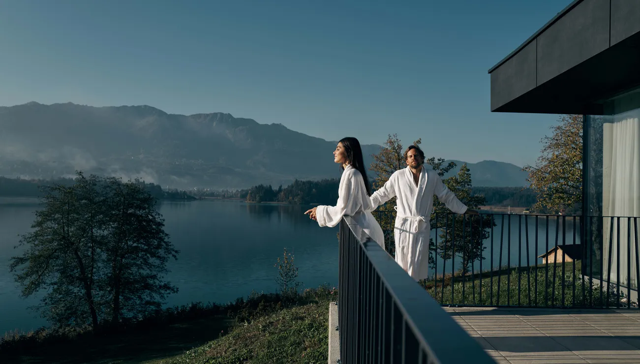 Couple in bathrobes enjoying lake and mountain view from spa hotel terrace