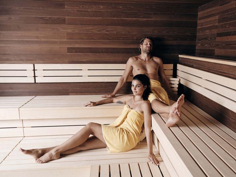 Uomo e donna che si rilassano in una sauna in legno con asciugamani gialli