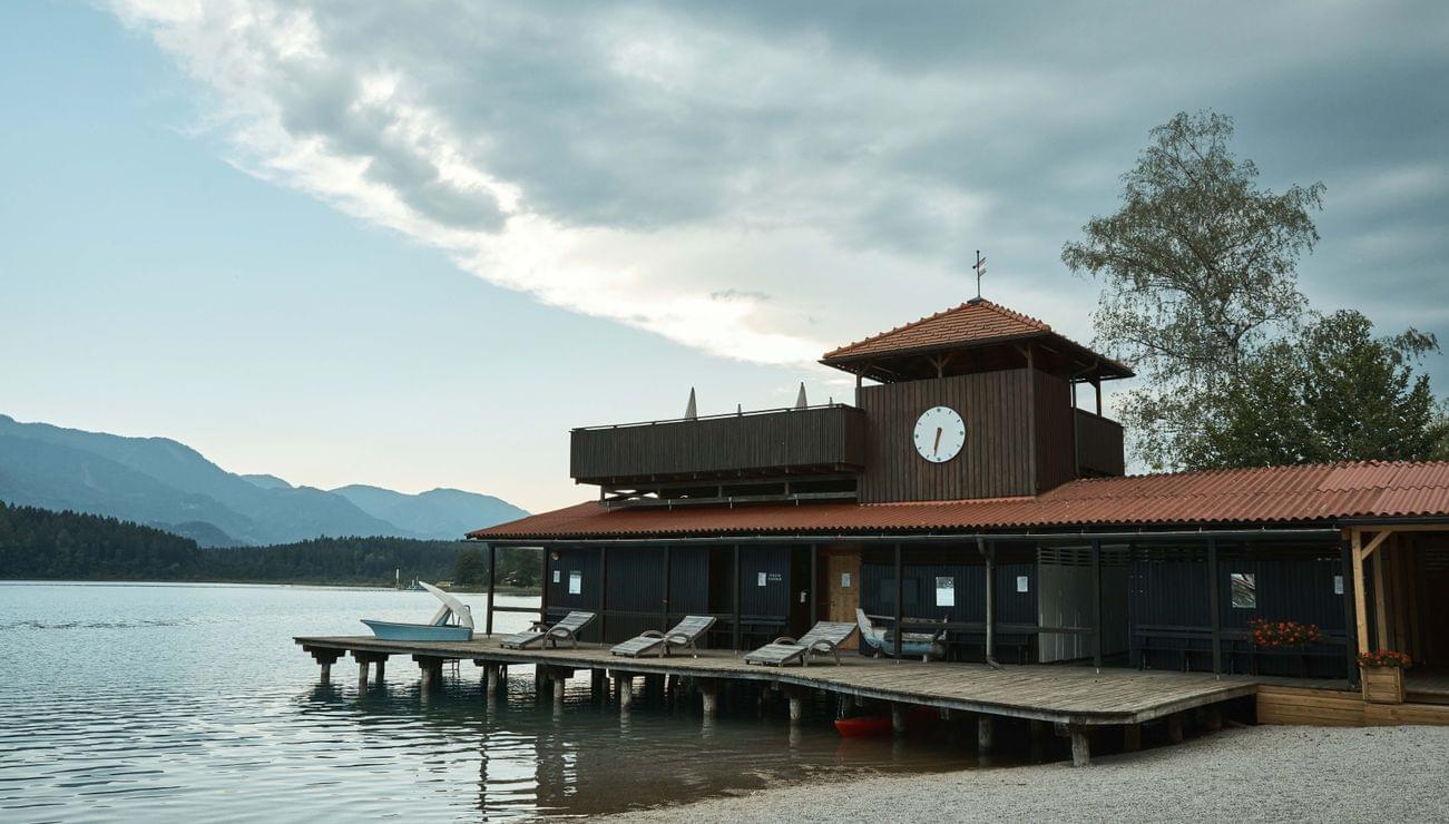 Holzbootshaus am See mit Uhrturm und Liegestühlen am ruhigen Wasser