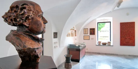 Bronzebüste in einem Museumsraum mit gerahmten Kunstwerken und historischen Exponaten