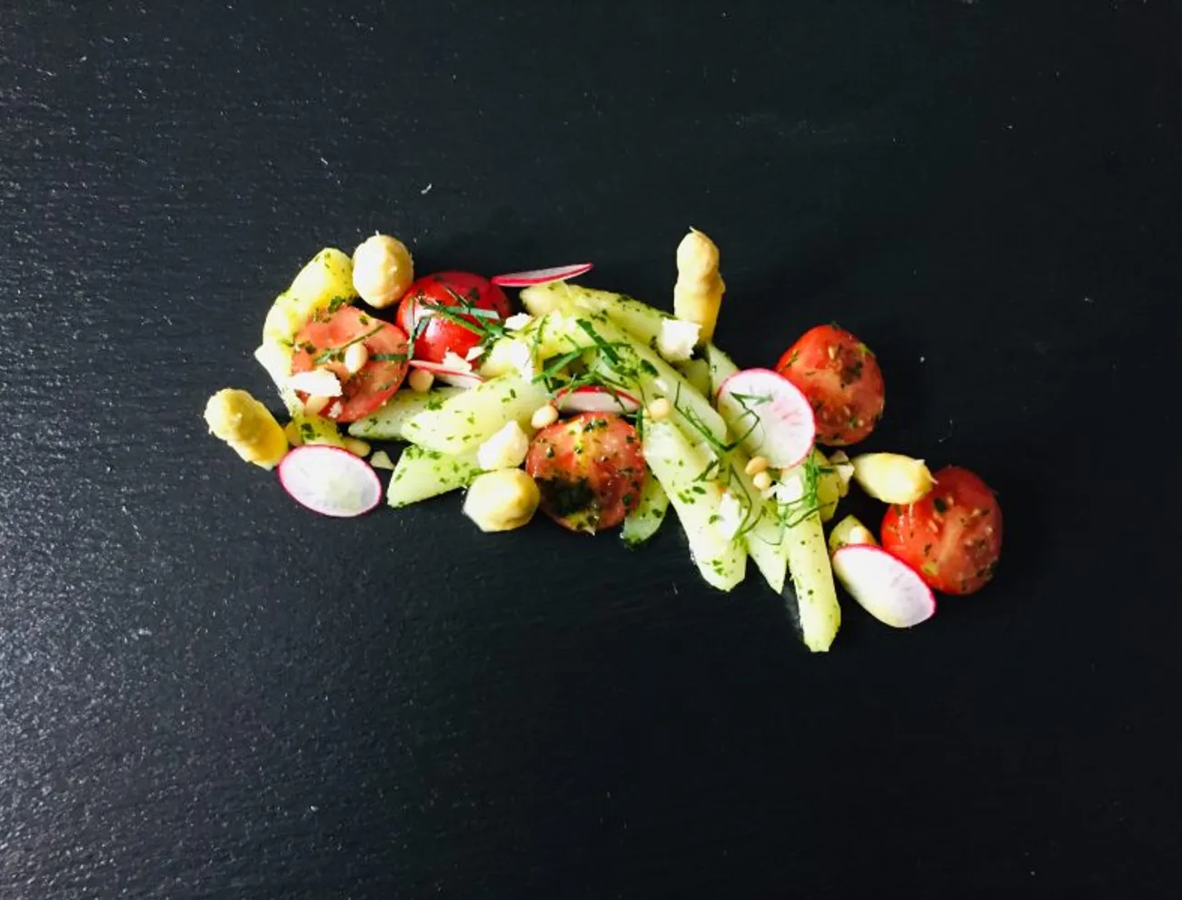 Gourmet-Kartoffelsalat mit Cherrytomaten, Radieschen und weißem Spargel auf schwarzem Schiefer