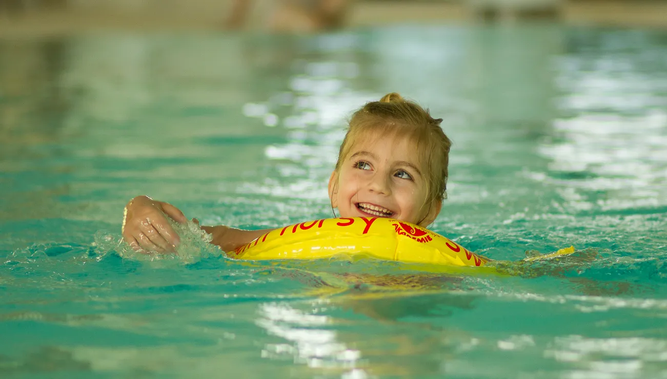 Lächelndes Kind schwimmt im Pool mit gelbem Schwimmreifen
