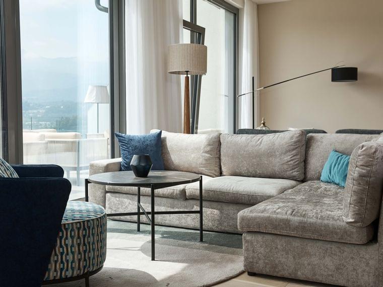 Modernes Wohnzimmer mit grauem Ecksofa, blauen Zierkissen und großen Fenstern
