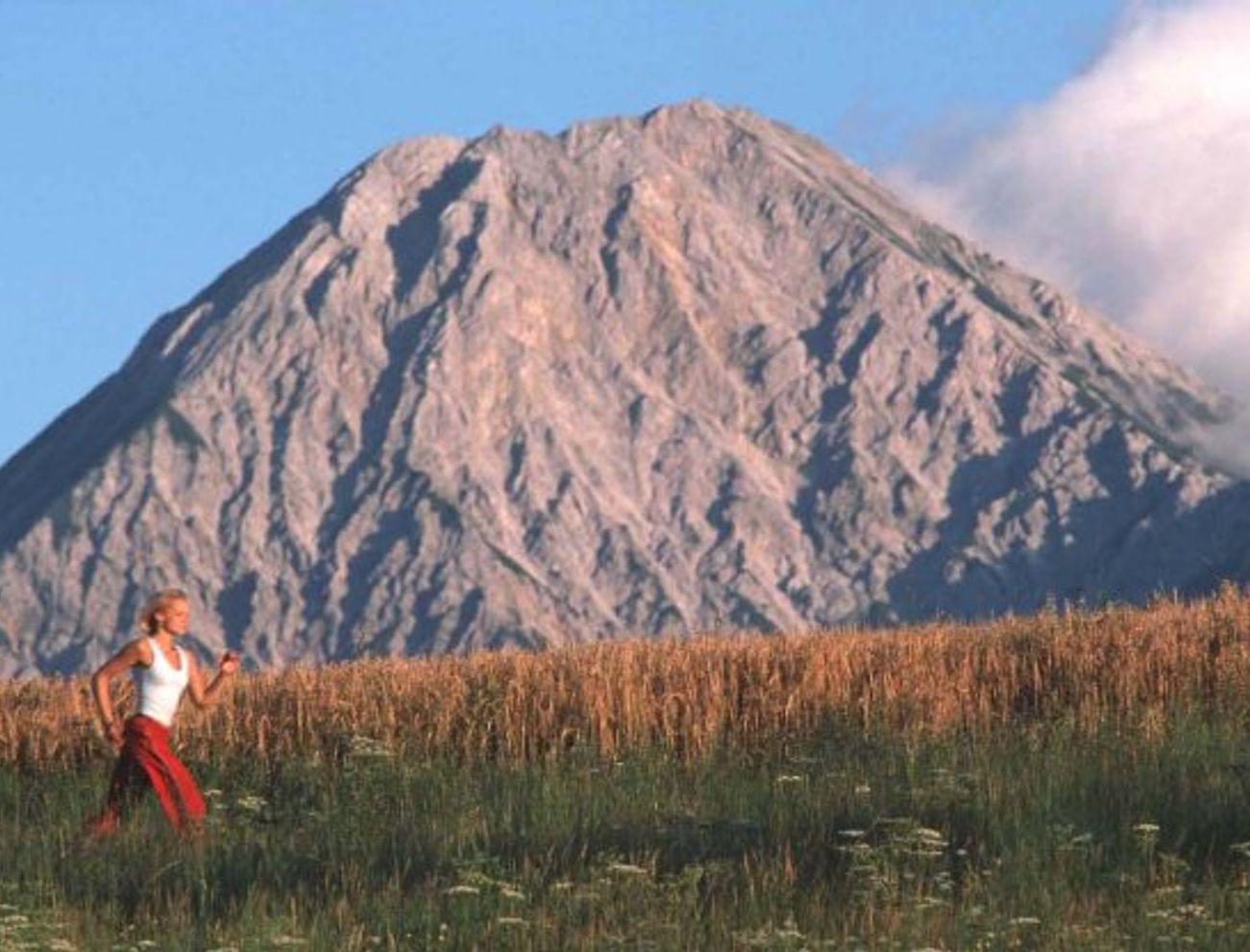 Frau joggt auf einer Wiese mit großem Berg im Hintergrund