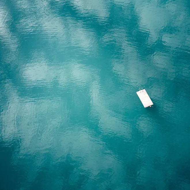 Schwimmender Holzsteg auf ruhigem türkisfarbenem See mit Himmelsreflexionen