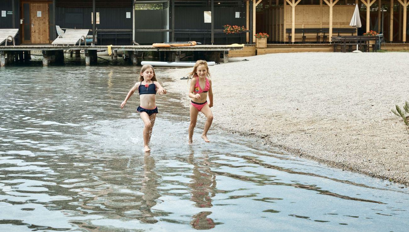 Due bambine in costume da bagno corrono nell'acqua bassa vicino a una cabina sul lago