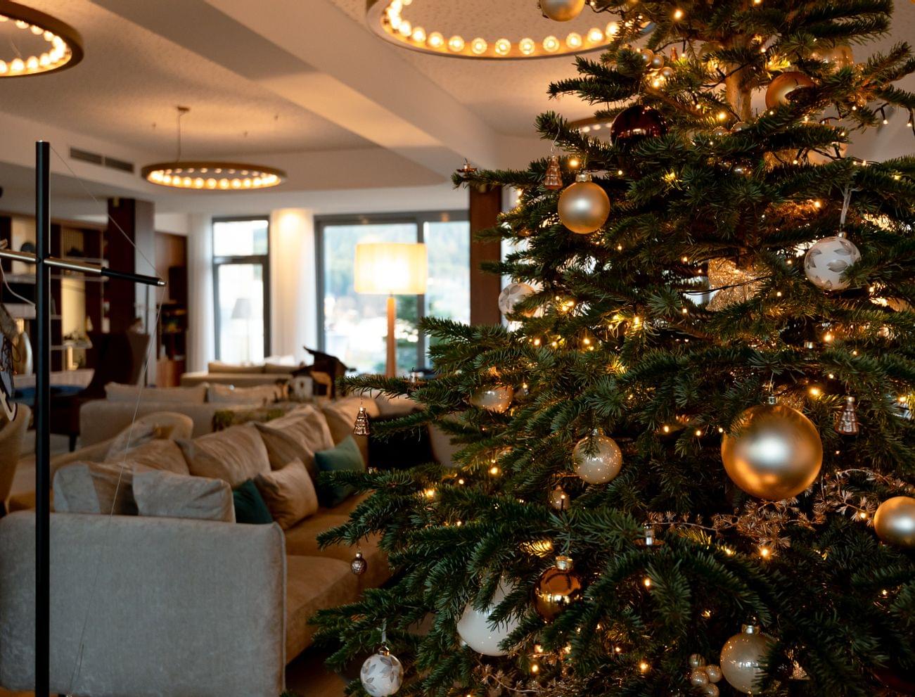 Eleganter Weihnachtsbaum mit goldenen Kugeln und Lichtern in einer gemütlichen Hotellounge
