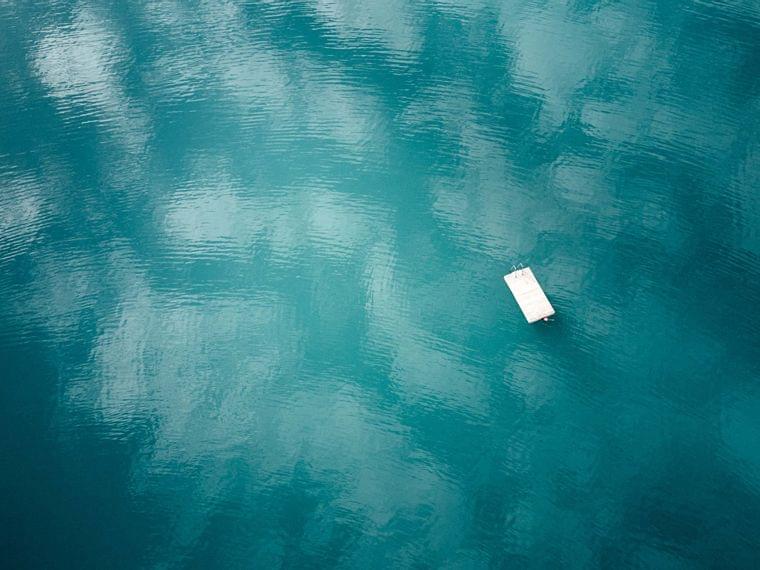 Schwimmender Holzsteg auf ruhigem türkisfarbenem See mit Himmelsreflexionen