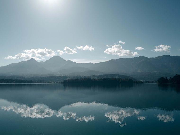 Lago di montagna calmo che riflette nuvole e cime sotto il sole brillante