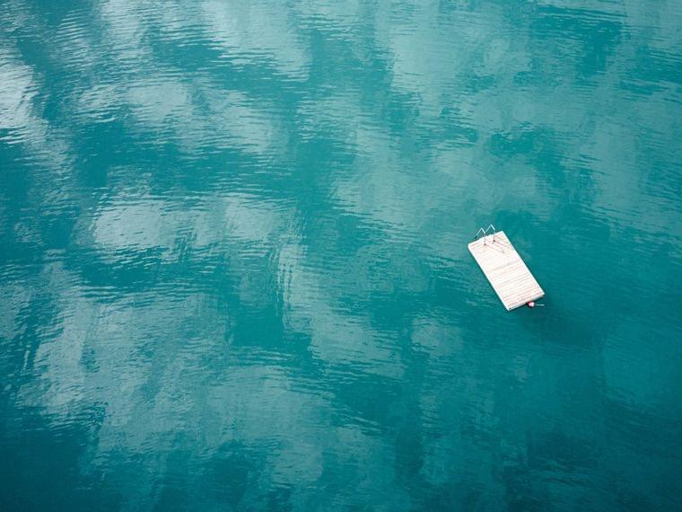 Schwimmender Holzsteg auf ruhigem türkisfarbenem See mit Himmelsreflexionen