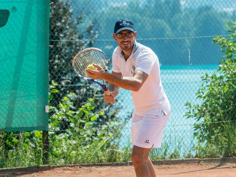 Mann in weißer Sportkleidung bereitet sich auf Aufschlag auf Sandtennisplatz vor