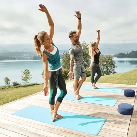 Gruppe beim Outdoor-Yoga auf Matten mit Seeblick bei sonnigem Wetter