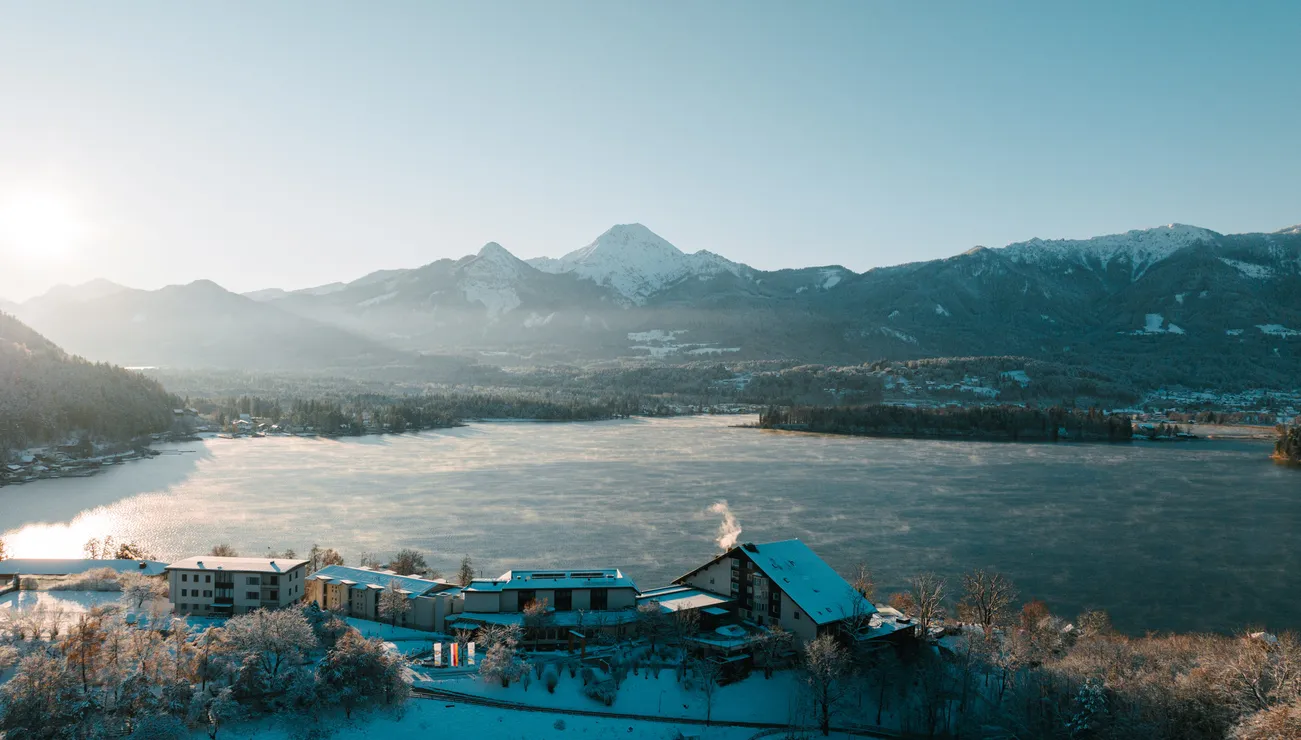 Villaggio innevato sul lago con montagne alpine e alba in paesaggio invernale