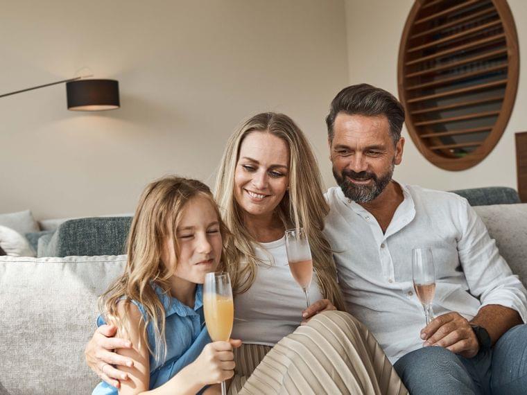 Happy family sitting on sofa enjoying drinks together in cozy living room
