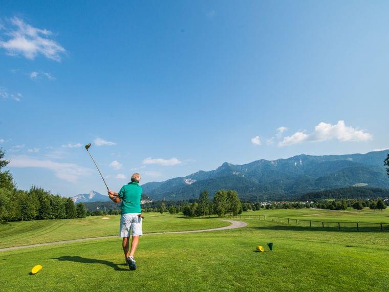 Golfer schwingt Golfschläger auf sonnigem Golfplatz in den Bergen im Sommer