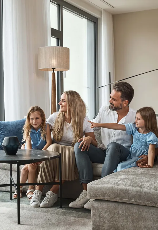 Famiglia felice seduta su divano moderno in soggiorno luminoso con vista montagna